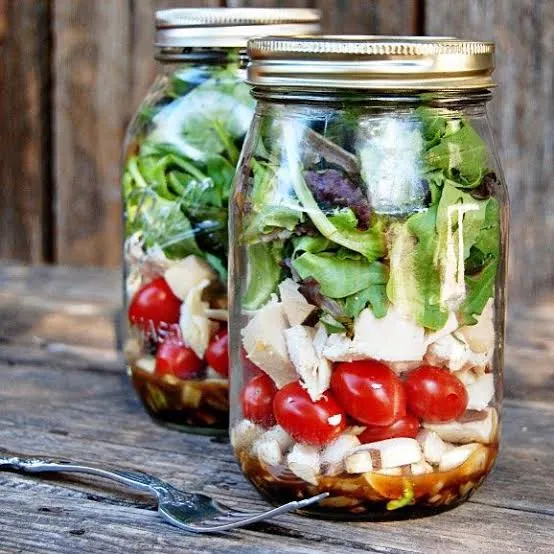 Dos ensaladas en frasco sobre una mesa de madera